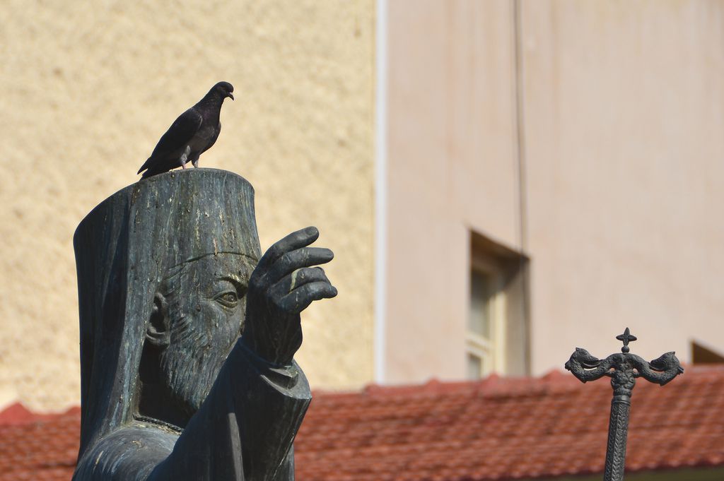 Bird perched on top of Greek Orthodox statue in Athens, Greece
